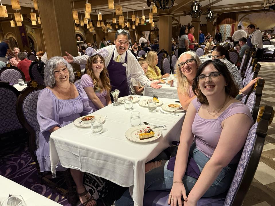 Dinner on our first Disney cruise: four women in purple sitting around a table with Rapunzel's lanterns up top and the best server ever with his hands out
