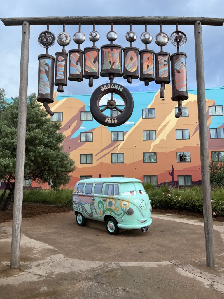 Fillmore in front of his sign with a resort in the background painted like the desert . Art of Animation Resort Review