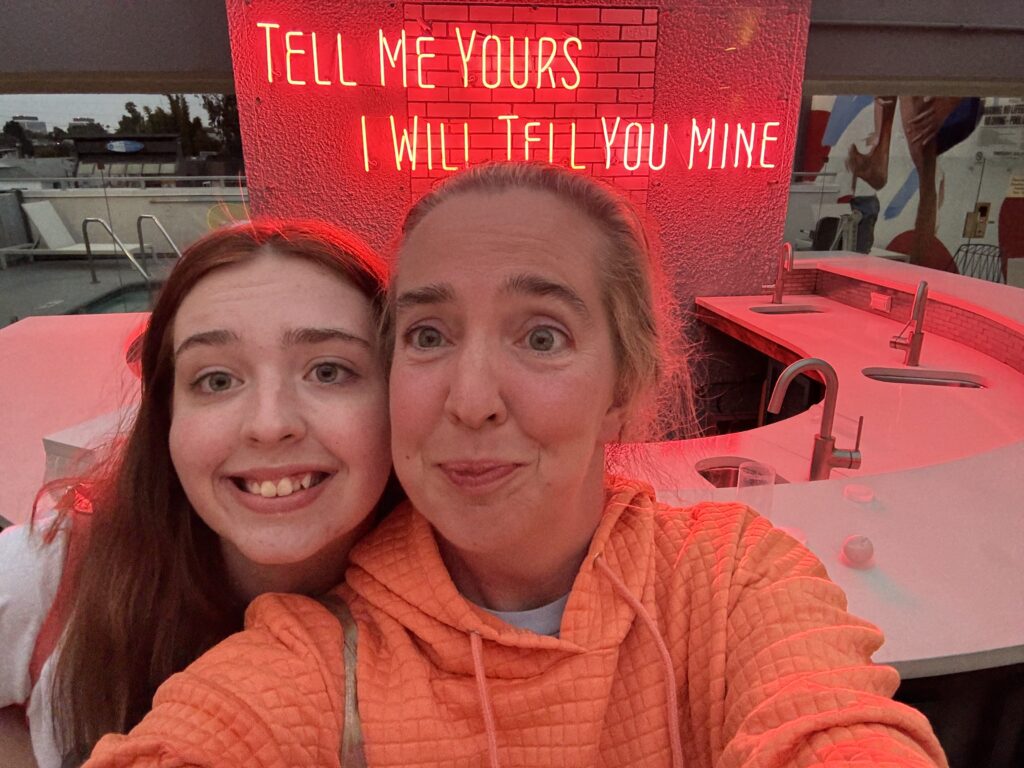 Two girls in front of a sign that says "Tell me yours and I will tell you mine"