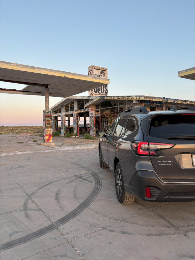 A subaru outback in front of an abandoned gas station with grafitti art on it