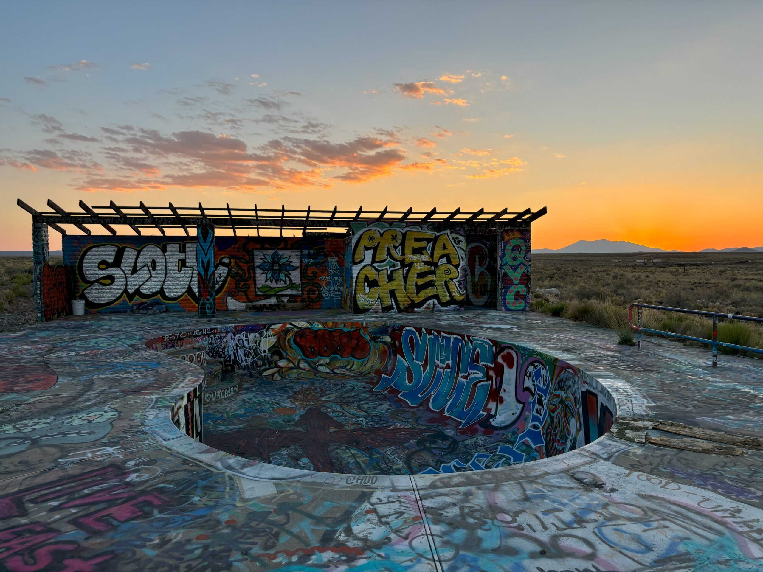 An abandoned pool that has been graffitied in front of a sunset in two guns, az